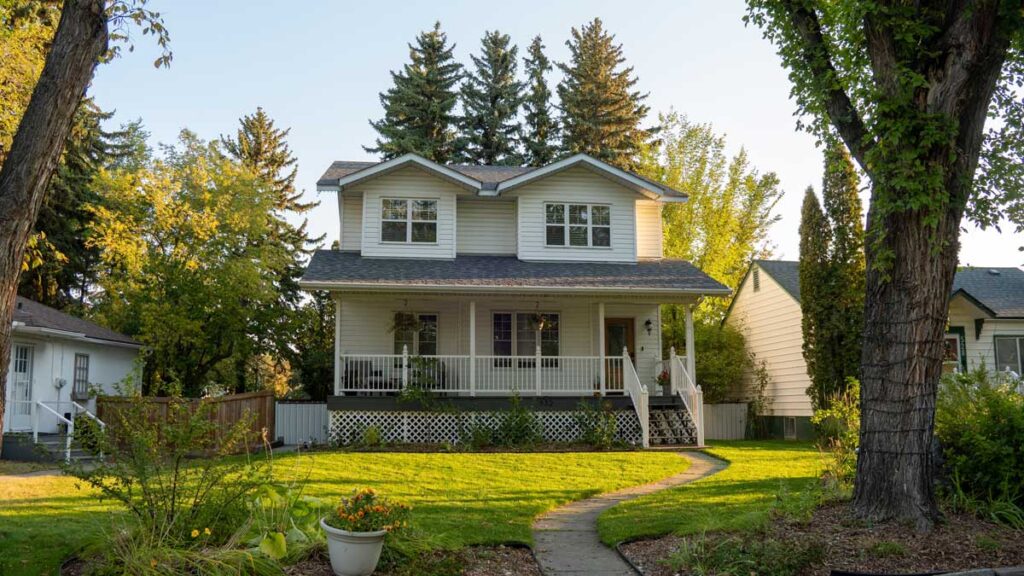 A two-story house, tiled roof, green lawn, and big trees around